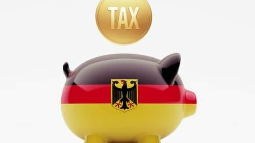 Une tirelire en forme de cochon aux couleurs du drapeau allemand et une pièce avec le mot taxe, pour représenter le système des impôts en Allemagne.